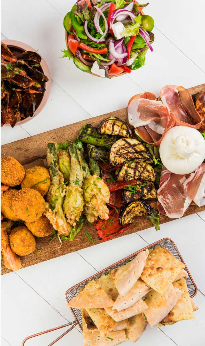 Colorful Italian Antipasto Platter with Burrata and Grilled Vegetables Overhead view of an Italian antipasto platter with grilled vegetables, cured meats, burrata cheese, fried appetizers, fresh salad, mussels, and focaccia bread.